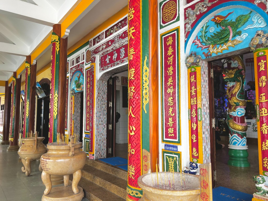 A Vietnamese temple with Chinese characters painted on bright red columns.