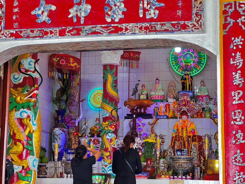 Two women in black, praying in front of many statues